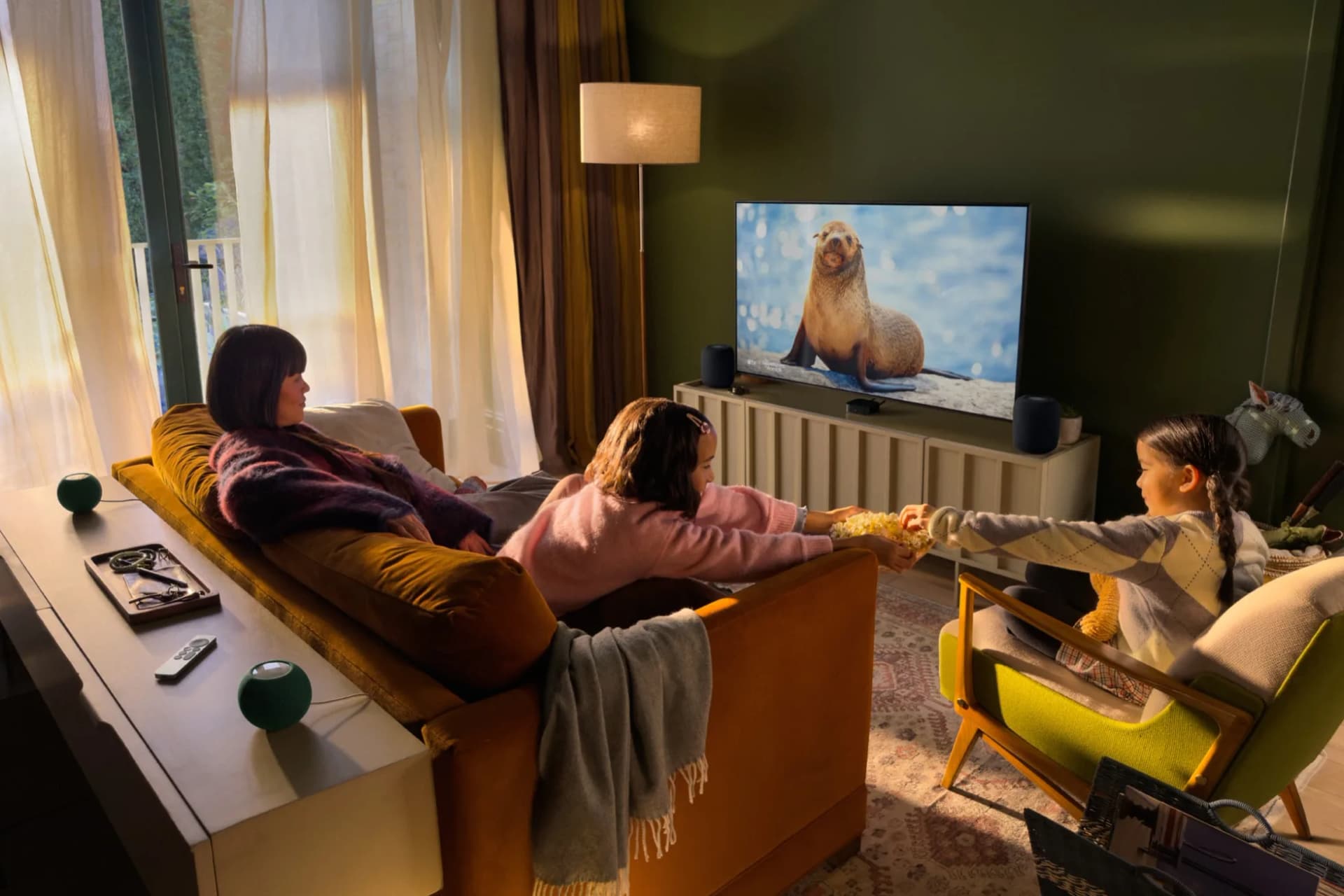 Apple TV 4K ve dört HomePod mini ile kurulmuş ev sineması düzeninde film izleyen aile